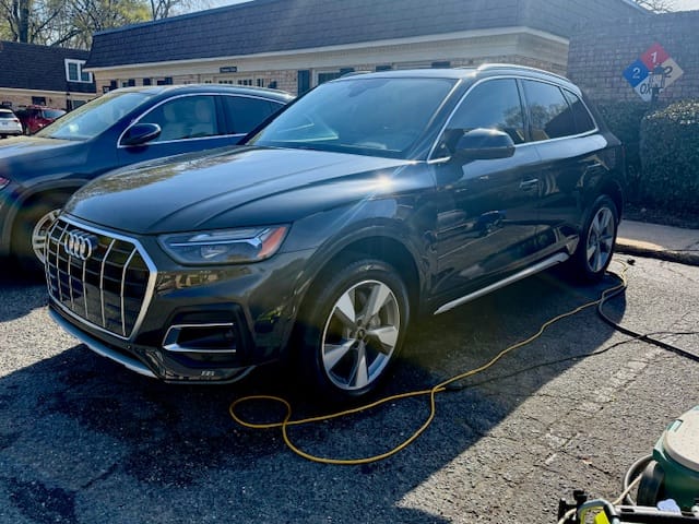 Dark grey Audi Q5 mid-wash on a customer driveway with hose visible